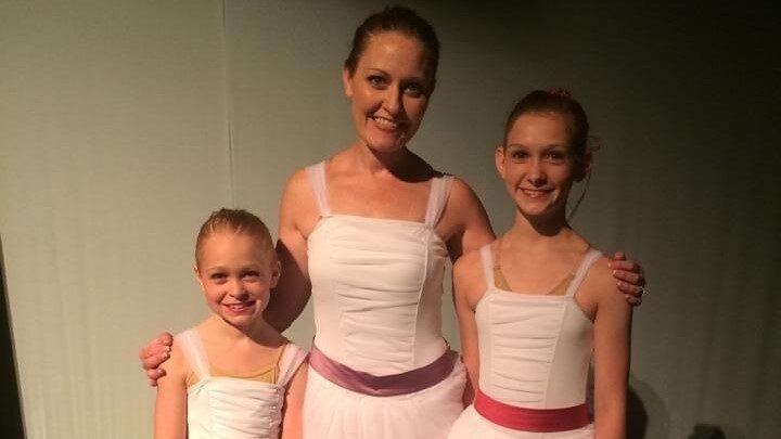 woman smiling with two girls in ballerina costumes