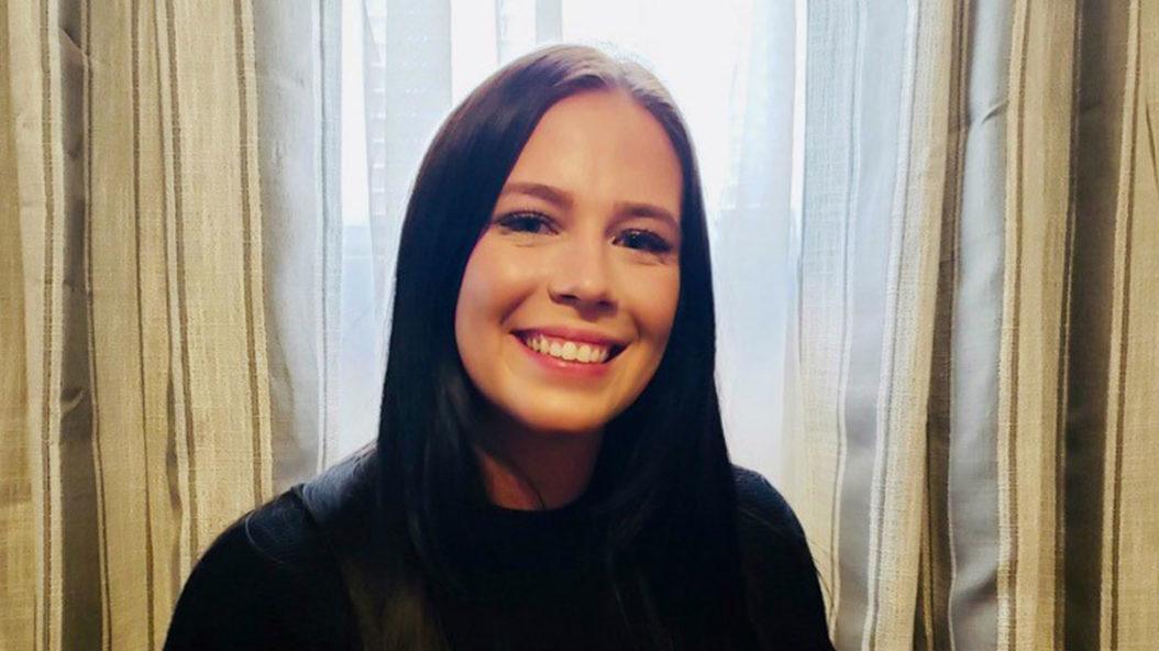 smiling young woman with dark hair wearing a black top against a wall of tan and white curtains